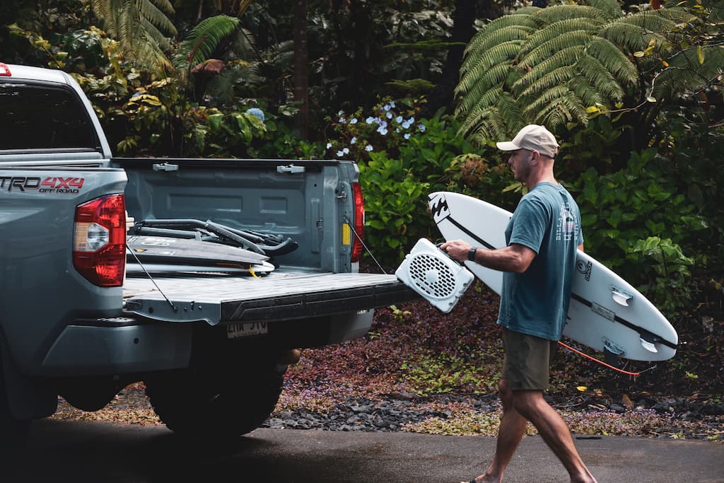 A lifestyle photo of Shane Dorian putting the white Original speaker on the back of a truck with a surfboard on his arm #speaker-color_white