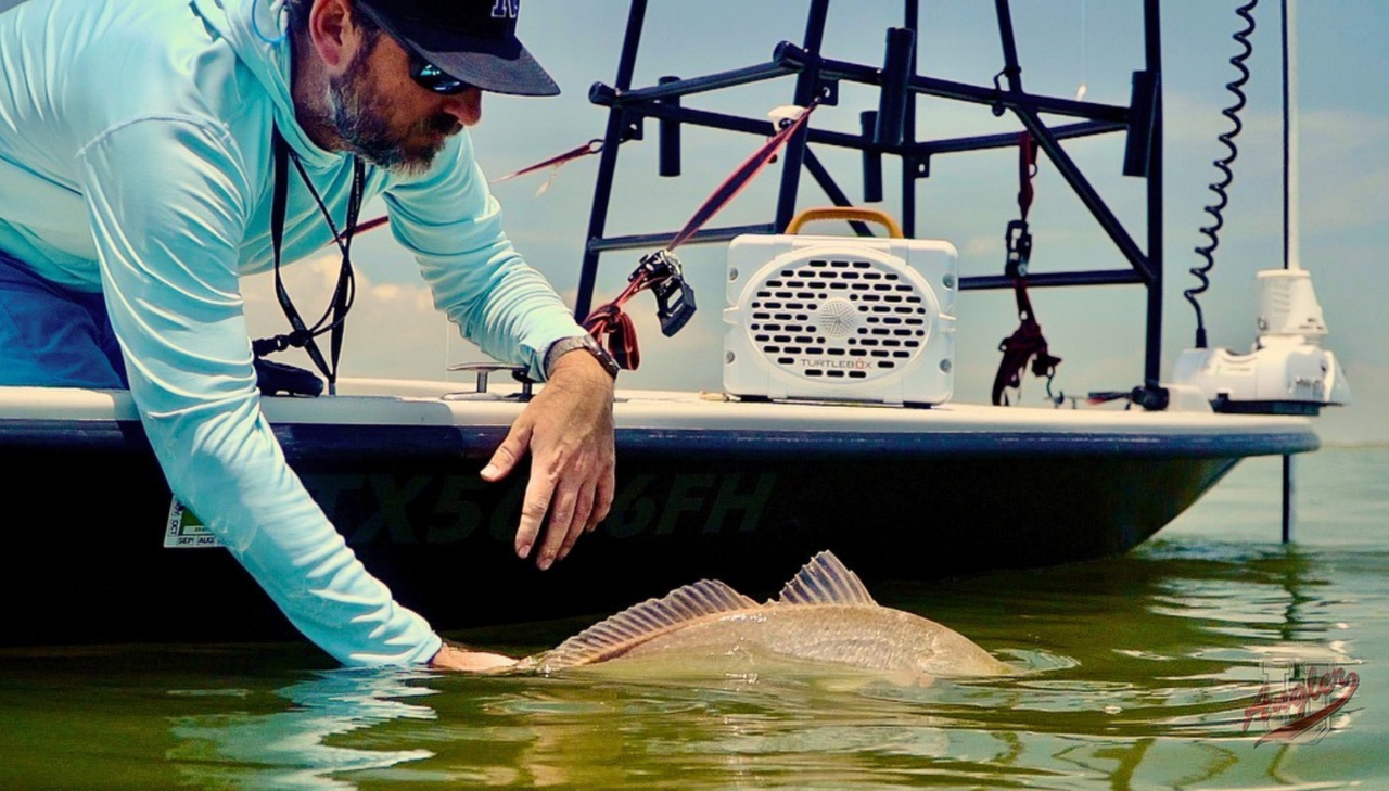 Caleb releasing a fish with his White Original Turtlebox on his boat