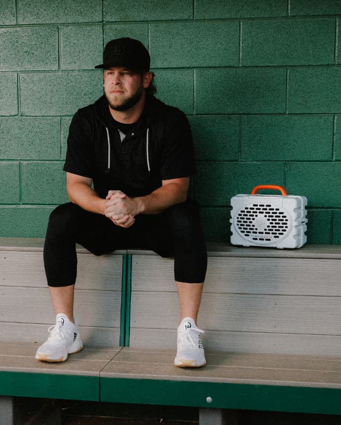 A J Minter sitted in a bench with his Turtlebox Original speaker in white color with blaze orange handle
