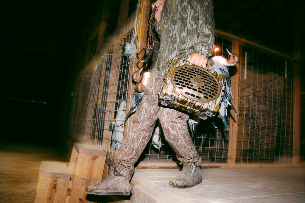 A person in camouflage clothing walks along a wooden structure at night while carrying a camouflage-patterned hunting blind.