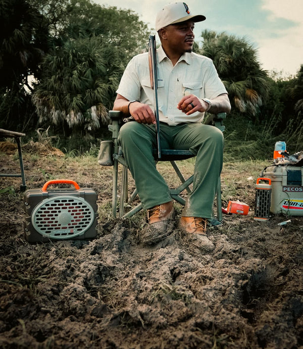 Man sitting on a chair in a muddy field with outdoor gear around him