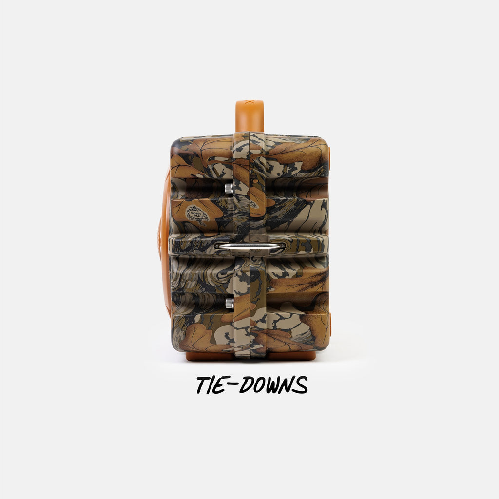 A camouflage-patterned backpack with tan straps and a tan top handle, shown against a light gray background with the text 'TIE-DOWNS' underneath.