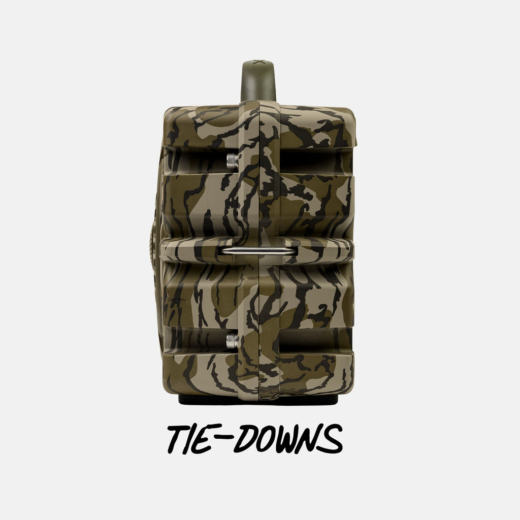 A camouflage-patterned game camera with a top-mounted lens and a metal ring for tie-down, shown against a light gray background with the text 'TIE-DOWNS' underneath.