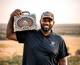 Lifestyle photo of a man holding a white Turtlebox on his shoulder, wearing an Everyday Camo Trucker Hat