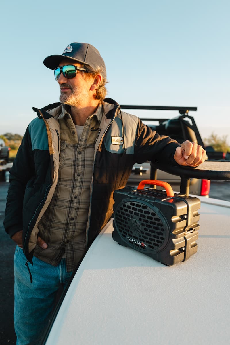 JT Van Zandt using a hat an sun eyeglasses listening music from a Turtlebox Original speaker in gray color with blaze orange handle