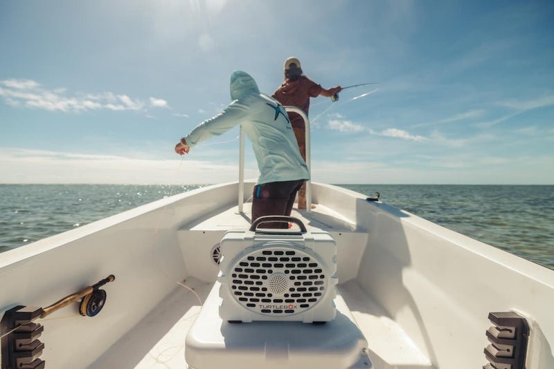Two guys fishing in a boat listening music from a Turtlebox Original speaker in white color