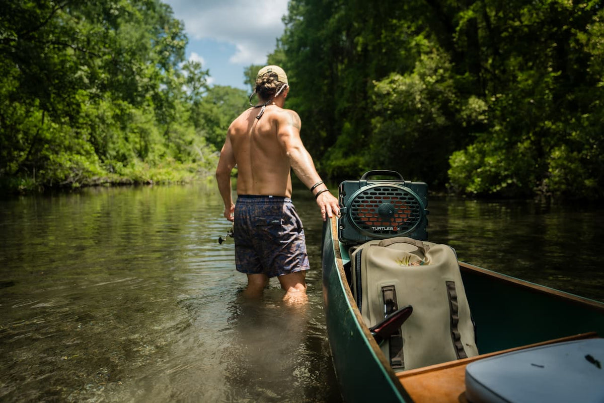 A lifestyle photo of a man in a river pulling his boat with a Turtlebox Original speaker in green attached to the boat #speaker-color_green