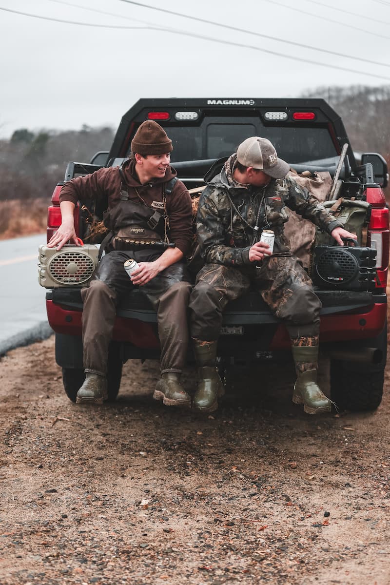 Two guys in a back truck with two Turtlebox Original speakers in tan and gray colors
