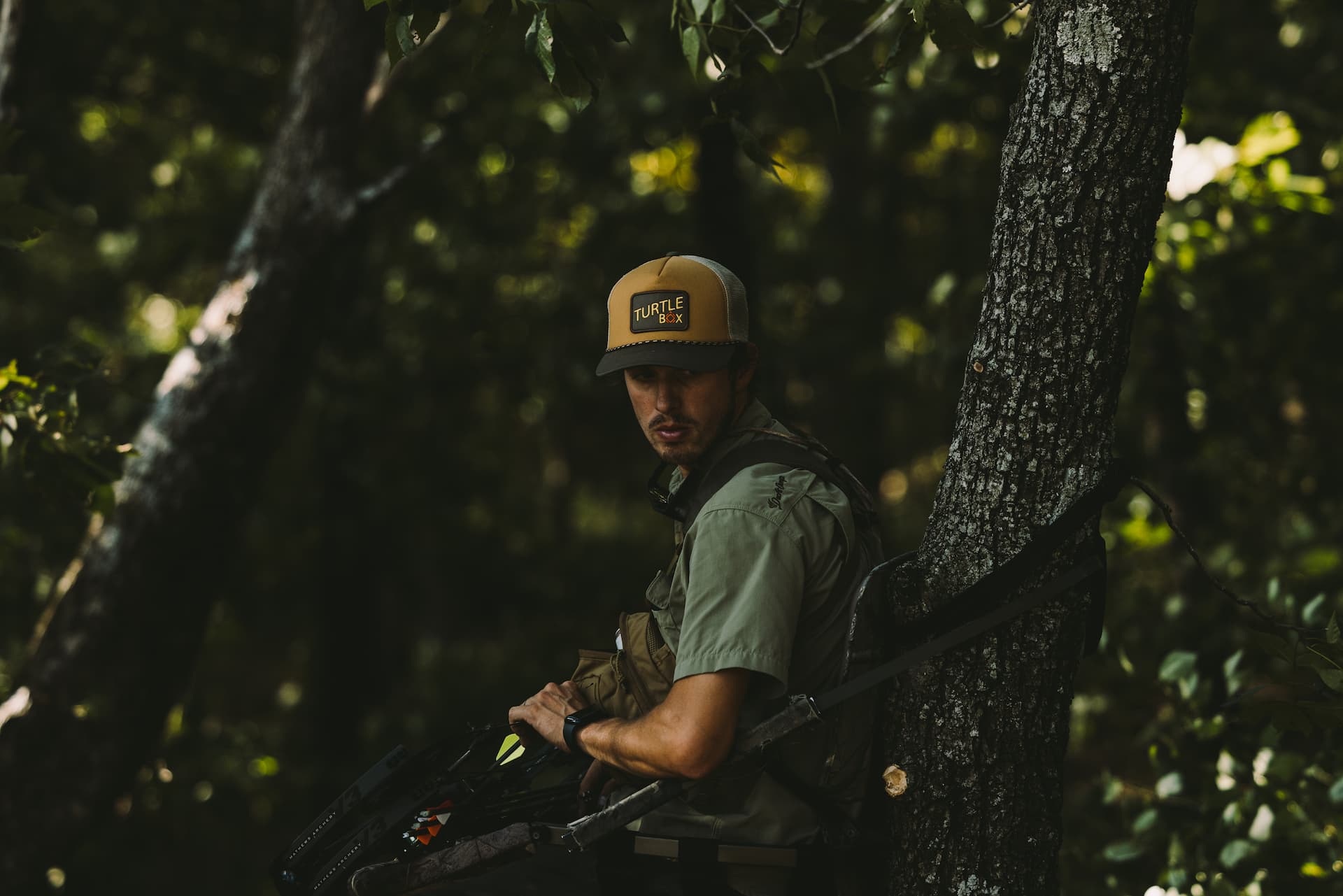 A guy in a tree with a Turtlebox hat and his bow and arrows