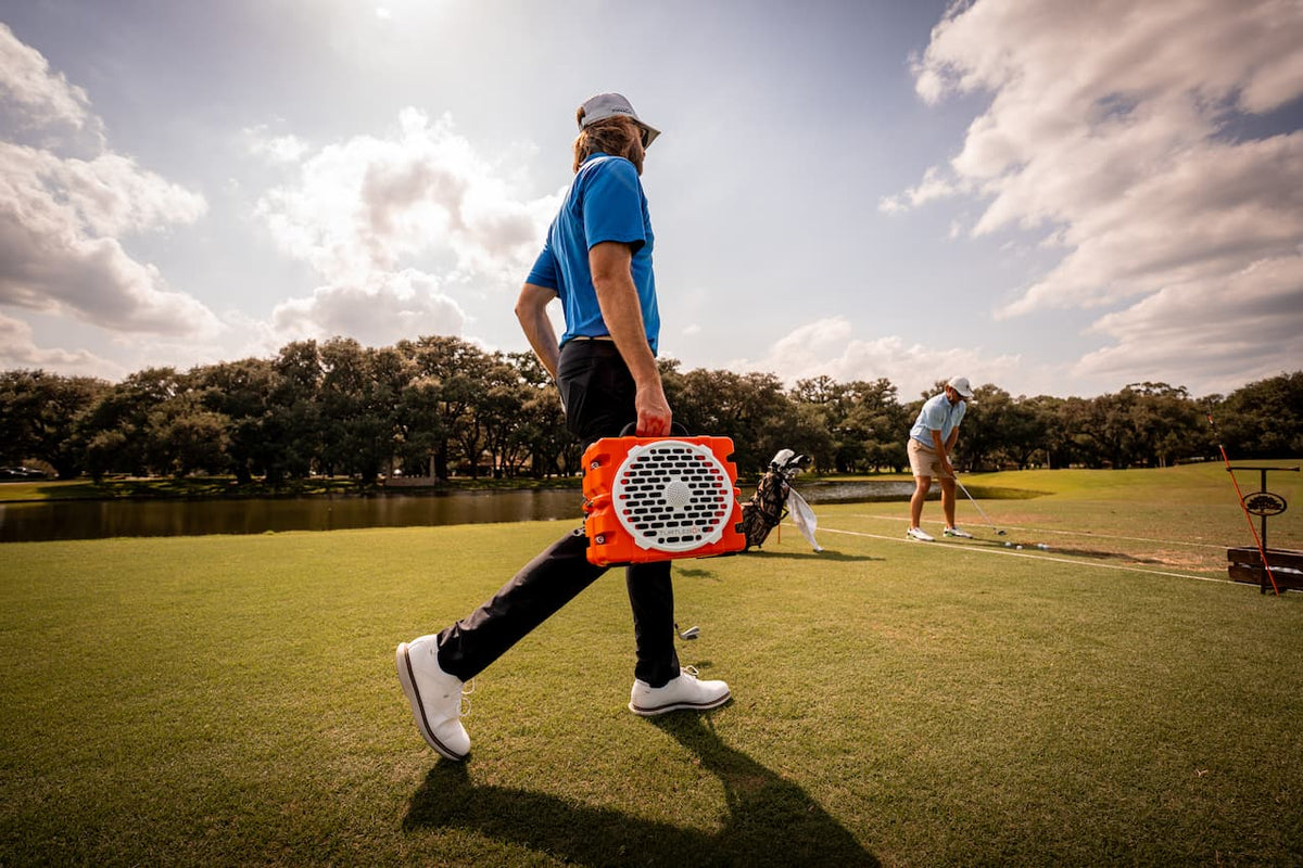 A lifestyle photo from a golfer walking with a Grande speaker orange #speaker-color_orange