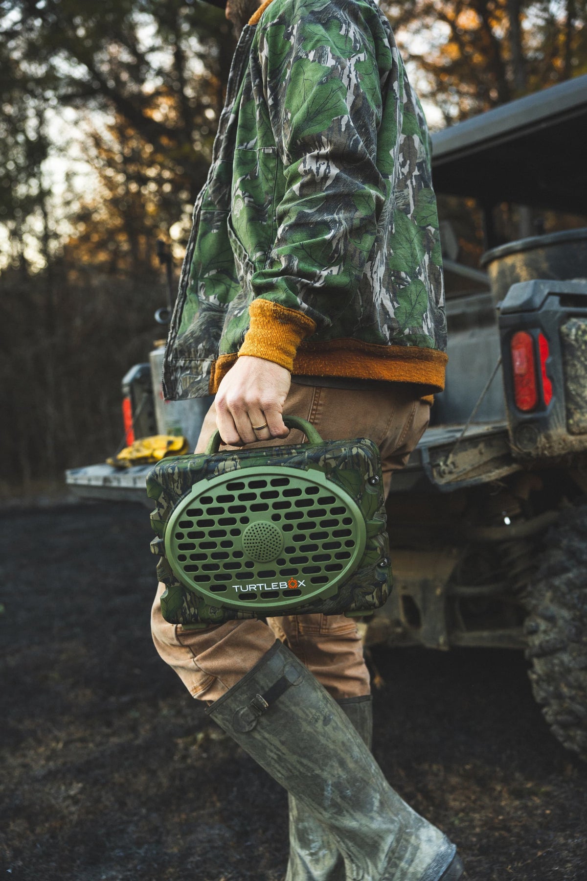 A lifestyle photo of a man holding a Turtlebox Original Mossy Oak Full Foliage edition speaker #speaker-color_full-foliage