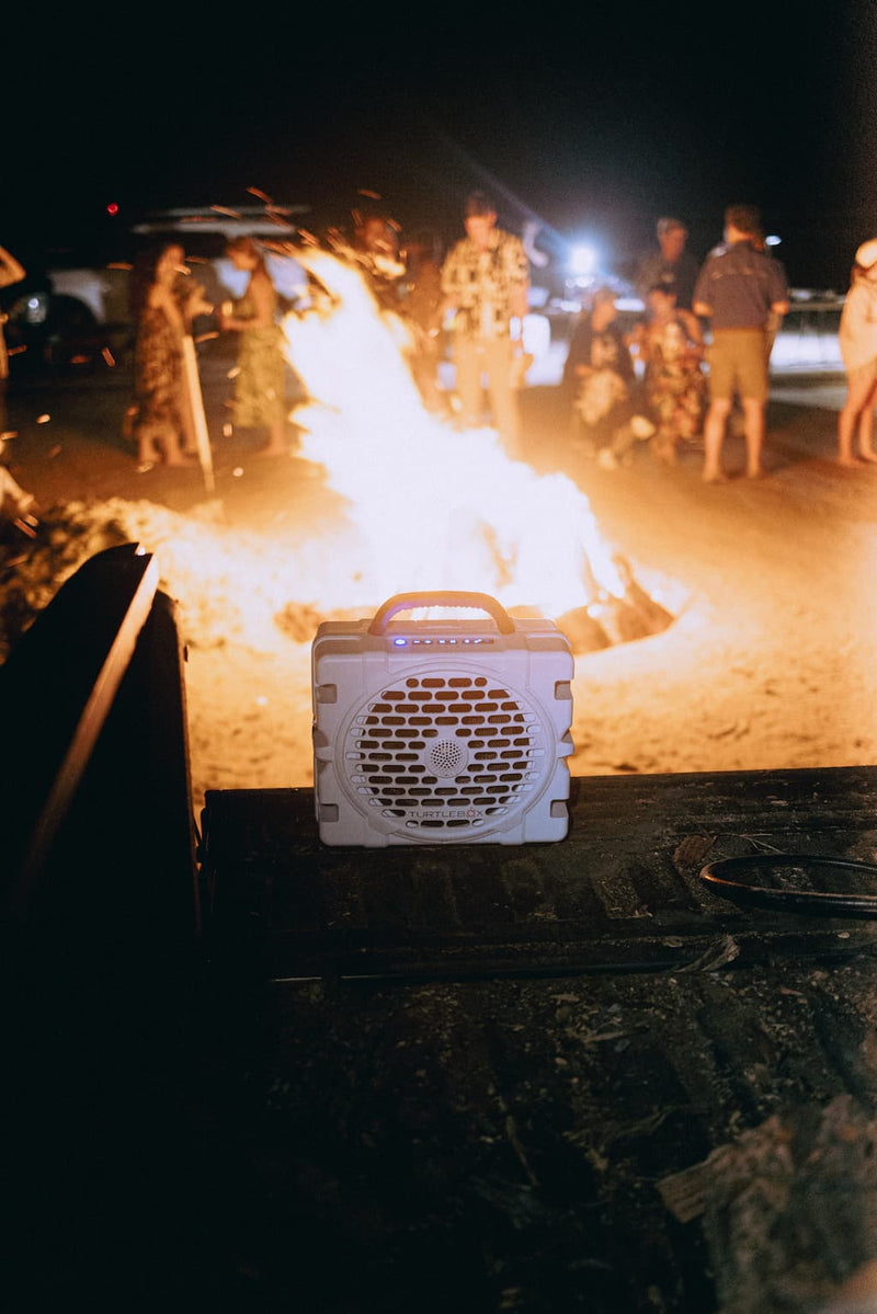 A lifestyle photo from a party with a big fire with people around and a Grande speaker in white playing music.