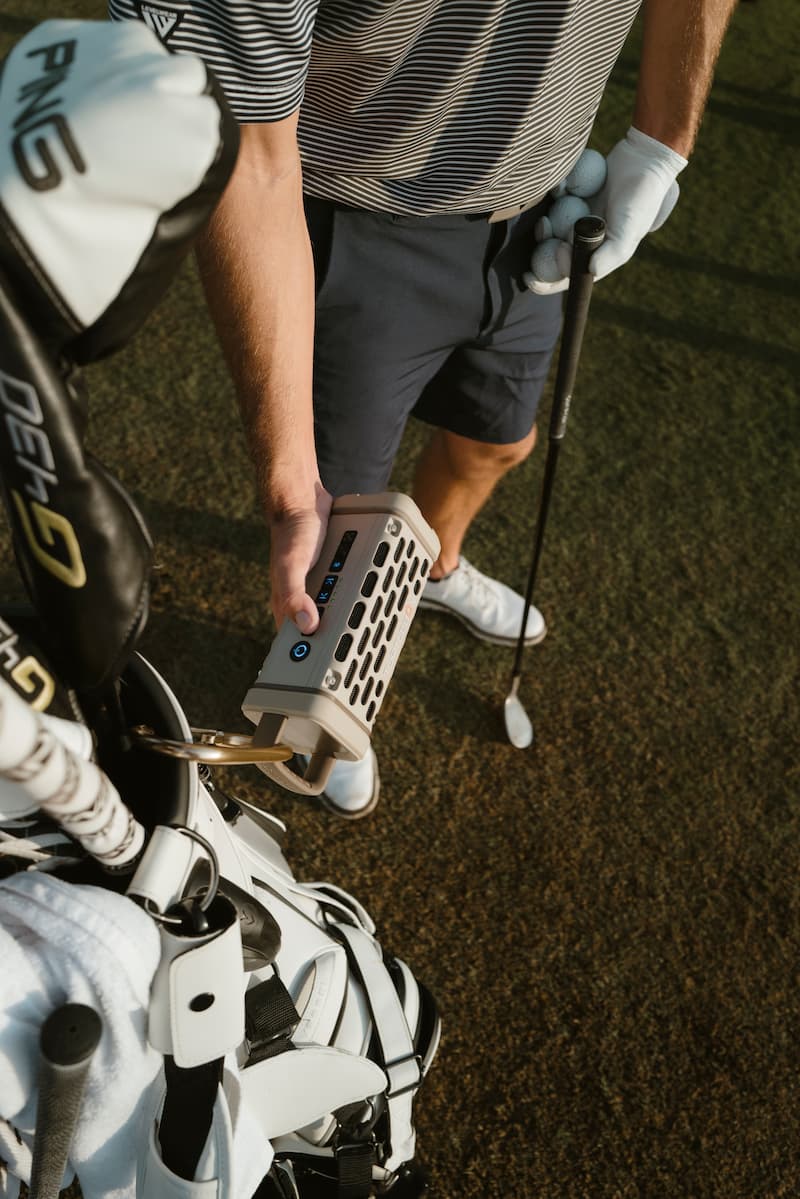 A guy increasing the volume on his Turtlebox Ranger speaker in tan color attached to his golf clubs bag