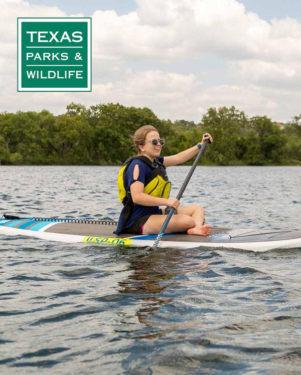 Woman sitting and paddleboarding in the water showing the Texas, Parks & Wildlife logo.