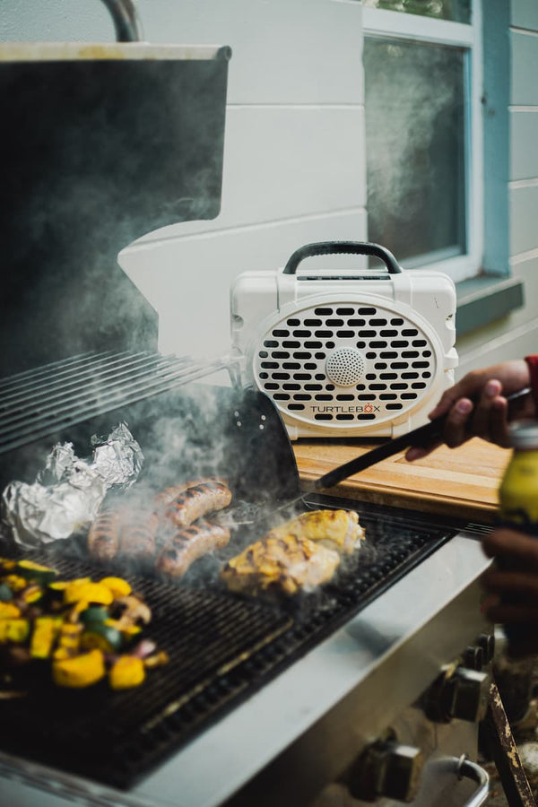 A Original speaker playing music besides a barbecue, where is grilling meat