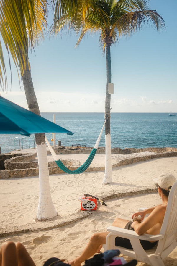 A guy listening music from a Original speaker in a beach with palm trees