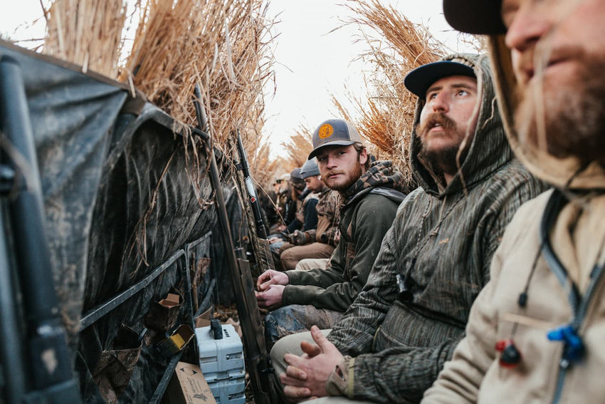 Group of hunters in camouflage gear sitting in a field with blinds.