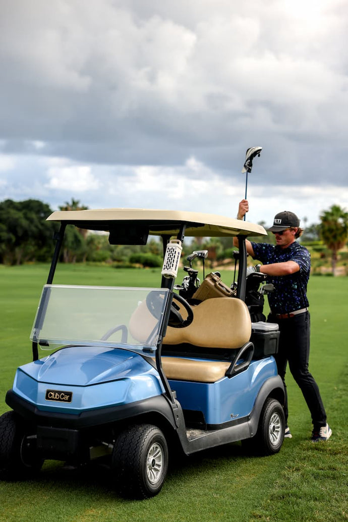 Person standing next to a blue golf cart on a golf course with a cloudy sky.
