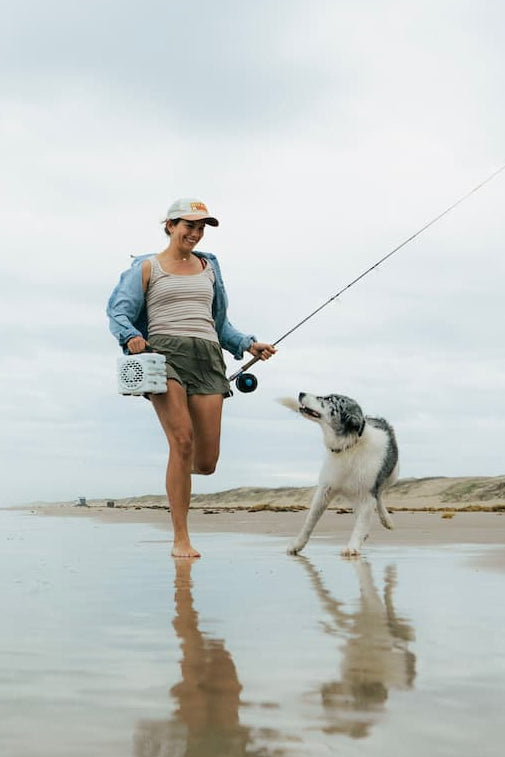 Two women and a dog fishing on a beach with a cloudy sky.