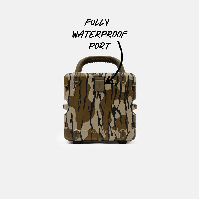 A rugged hard-shell case with a brown, beige, and black camouflage pattern, featuring a top handle and a metal port cover. Handwritten text above reads 'FULLY WATERPROOF PORT' with an arrow pointing to the metal port on the front.