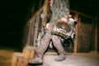 A person in camouflage clothing walks along a wooden structure at night while carrying a camouflage-patterned hunting blind.
