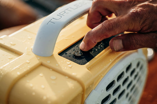 Hand pressing a button on a yellow and gray device with 'TURTLE BEACH' branding.