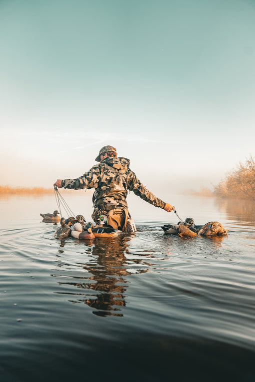 Person in camouflage gear with duck hunting decoys on a calm lake