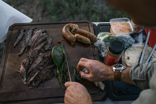 Person preparing food on a wooden cutting board outdoors