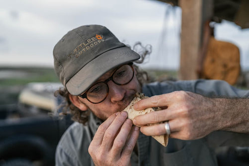 Person eating outdoors wearing a cap with a visible Turtlebox brand logo