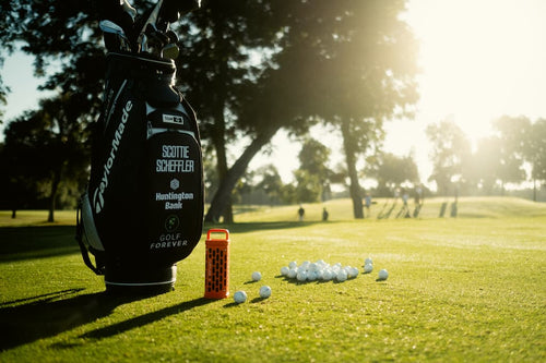 Golf bag with golf clubs and balls on a grassy field with trees in the background