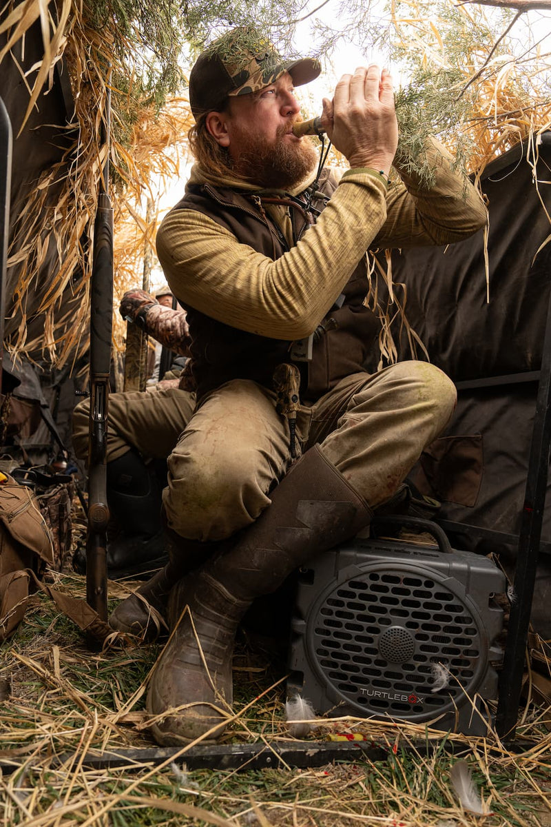 Man in hunting gear using a call device in a natural setting