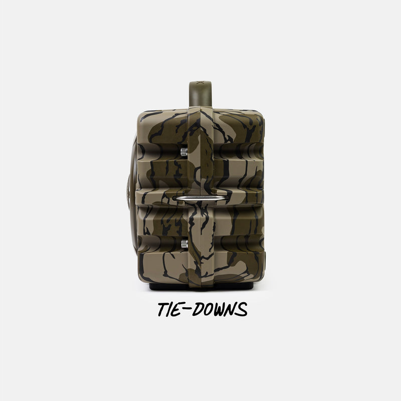A camouflage-patterned game camera with a top-mounted lens and a black 'TIE-DOWNS' text overlay below, set against a plain light gray background.