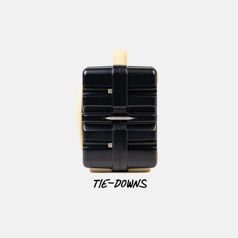 A black hard-shell suitcase with a beige handle and base, shown from the back with a black strap across the center. The text 'TIE-DOWNS' is printed below on a light gray background.