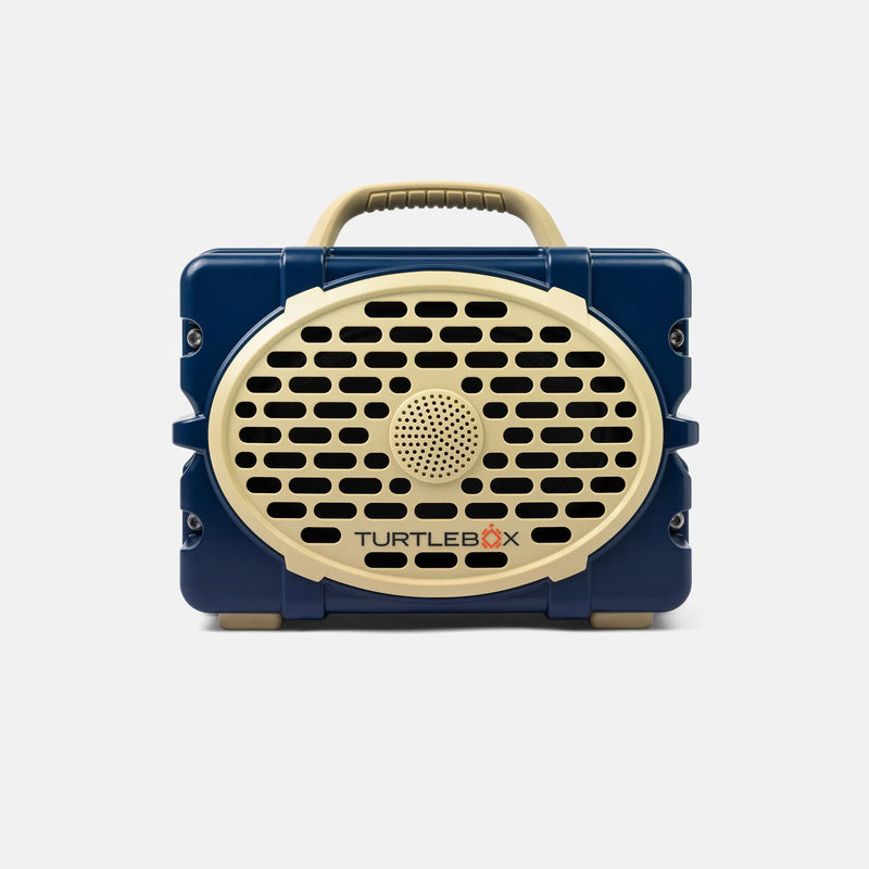 A retro-style portable speaker by TurtleBox, featuring a navy blue body with a cream-colored front grille, handle, and logo, shown against a light gray background.