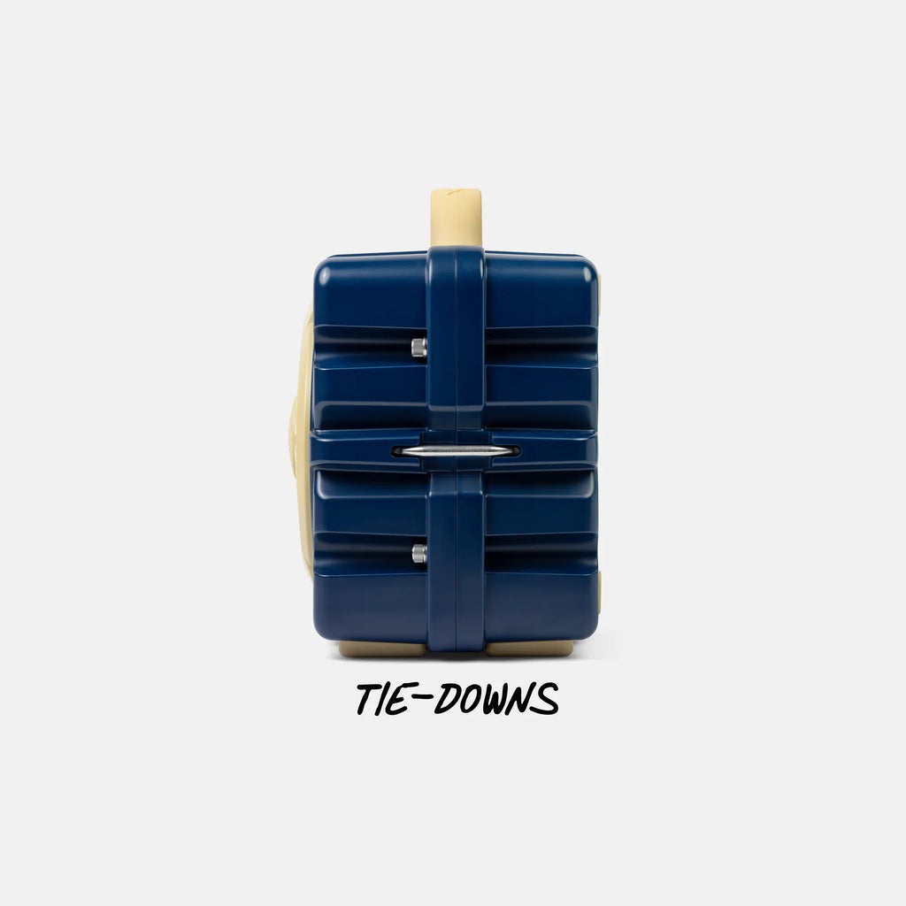 A navy blue hard-sided luggage-style bag with beige trim and a beige handle, shown from the back on a light gray background with the text 'TIE-DOWNS' below.