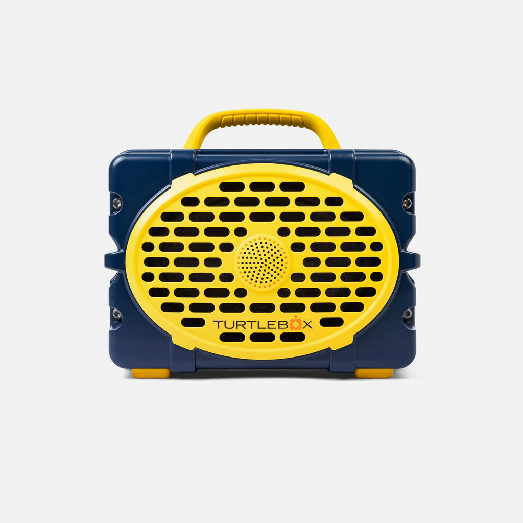 A portable Turtlebox speaker with a navy blue plastic body and bright yellow accents, including a handle, front grille, and small feet, shown against a light gray background.