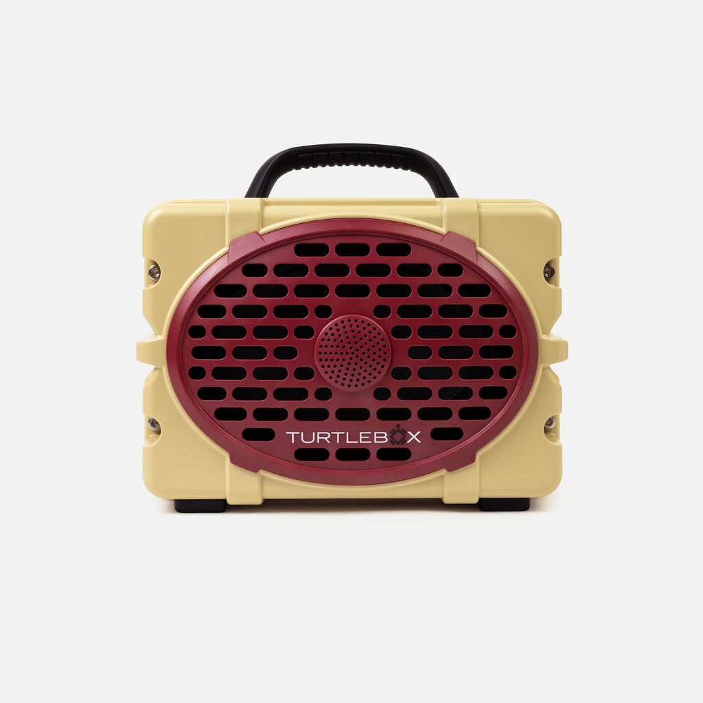 A retro-style portable speaker by Turtles X, featuring a cream-colored body, a prominent dark red oval front grille, and a black carrying handle, shown against a light gray background.