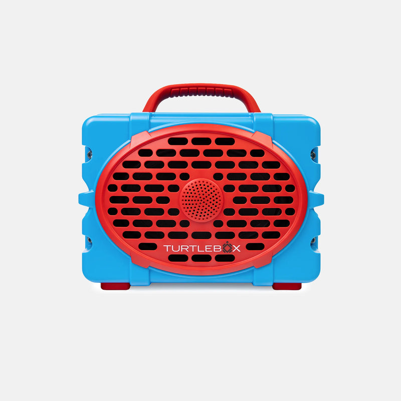 A blue and red portable speaker with a handle, shown from the front on a light gray background. The brand name 'TURTLEBOX' is printed on the red speaker grille.