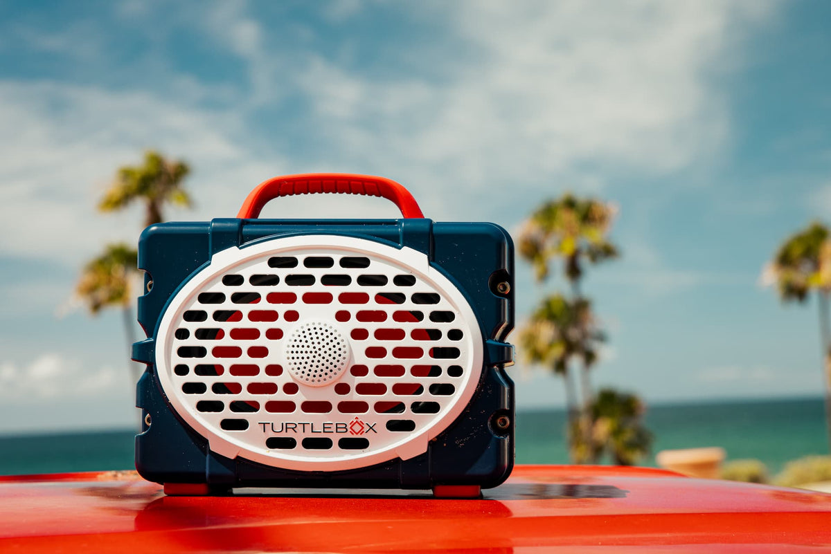 Turtlebox device on a red surface with palm trees and ocean in the background