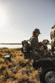 A lifestyle photo of two hunters with a dog on an ATV near a body of water with a Delta Turtlebox Ranger speaker attached to a backpack. #base-color_delta