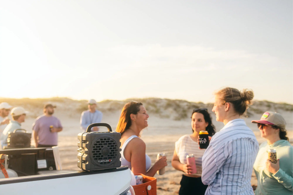 Group of people socializing on a beach with a cooler and drinks.