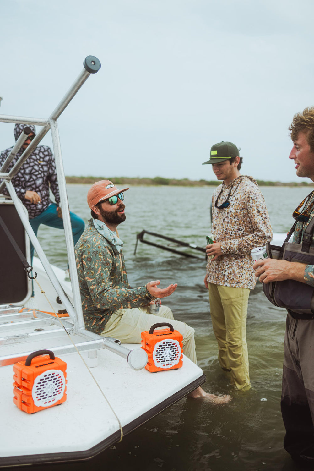 Group of people on a boat by a lake, with one person gesturing towards an orange speaker.