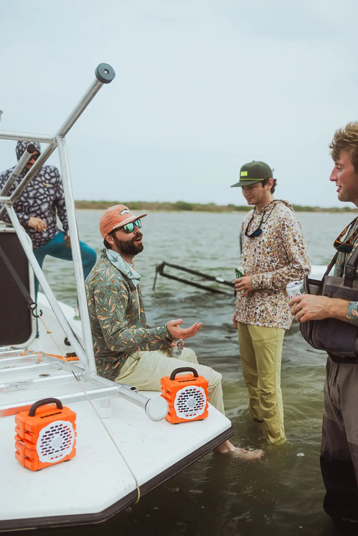 Group of people on a boat by a lake, with one person gesturing towards an orange speaker.