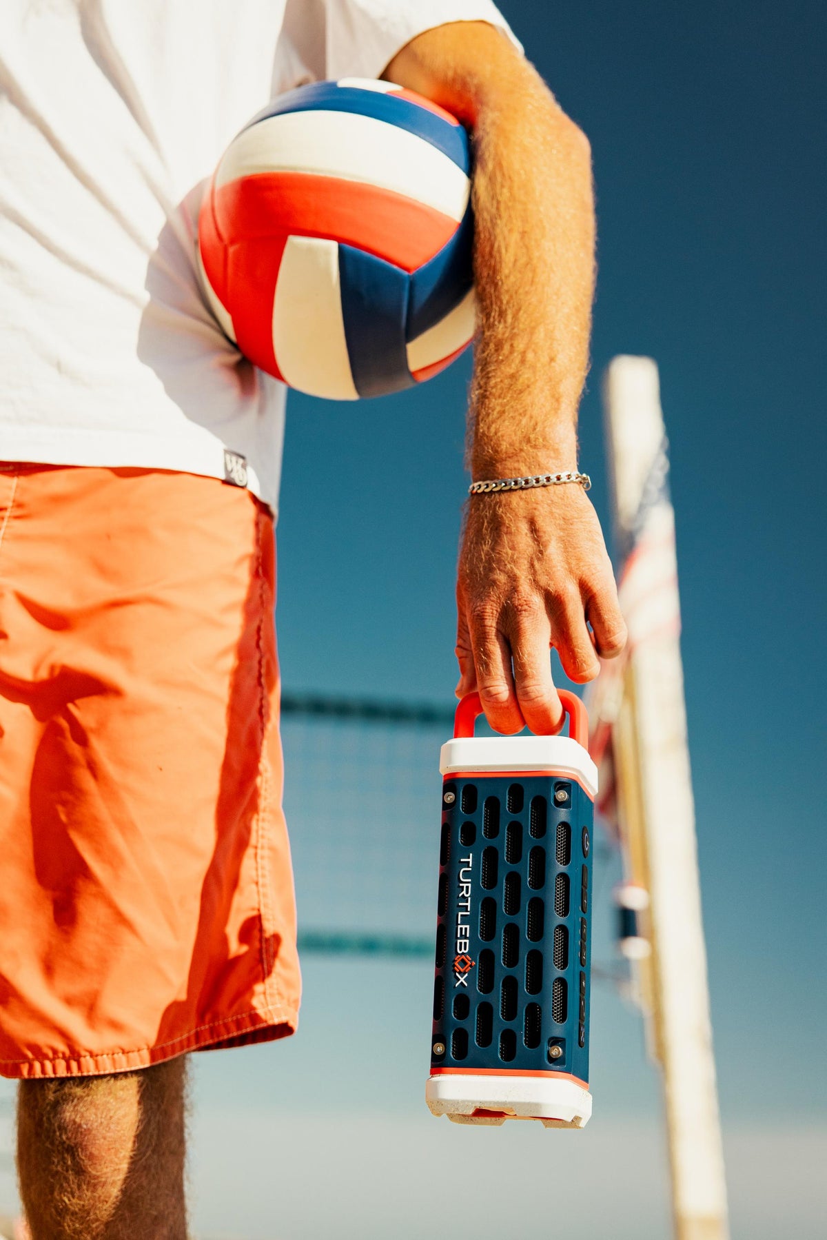Person holding a volleyball and a cooler with a blue sky background