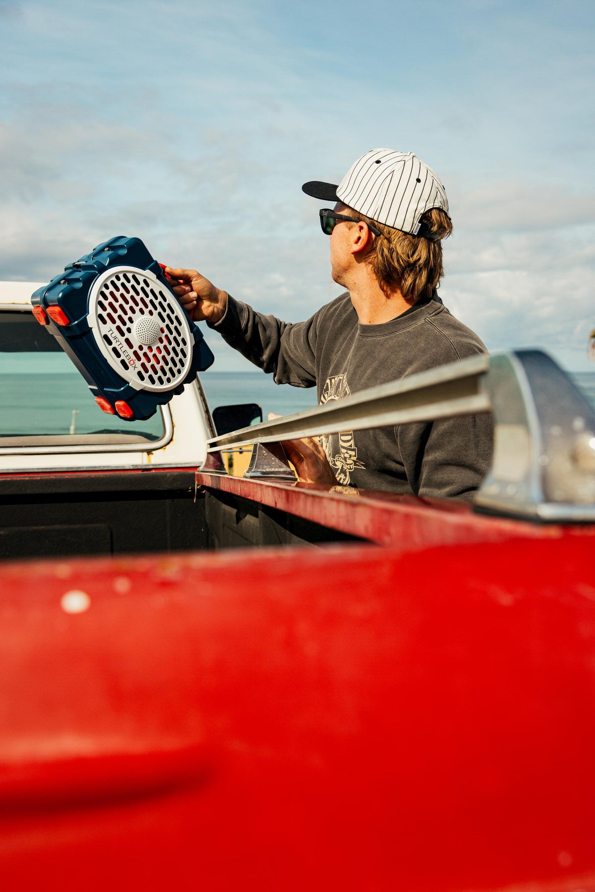 Person holding a large tool in the back of a red truck with a clear sky.