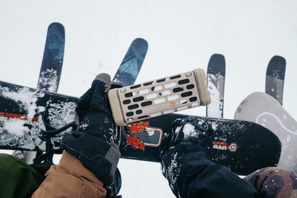 Person holding a Turtlebox Ranger in Tan color with skis in the background