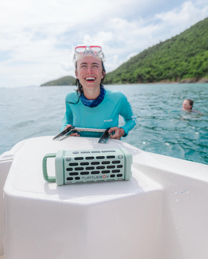 A girl climbing to the boat after doing snorkling, a Turtlebox Ranger speaker in River Rock color is playing on the boat.