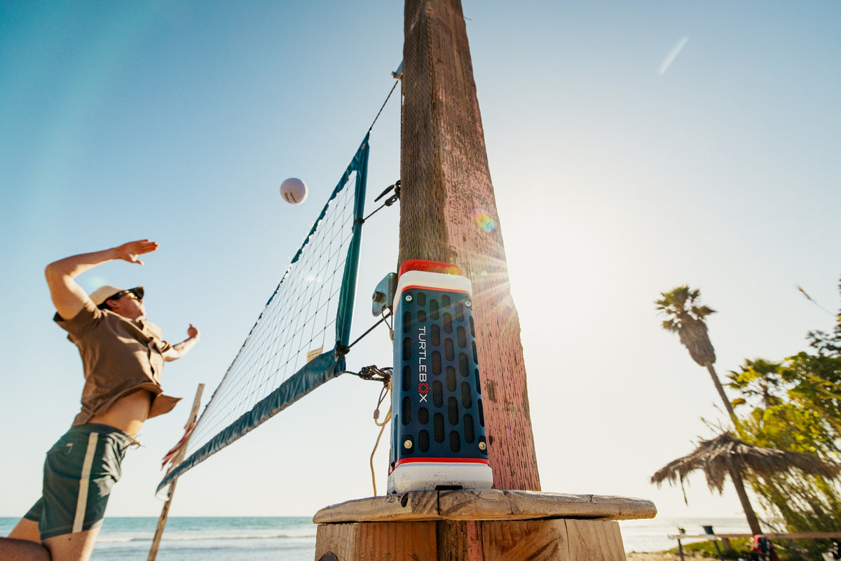 Person playing volleyball on a beach with a colorful volleyball net and ball.