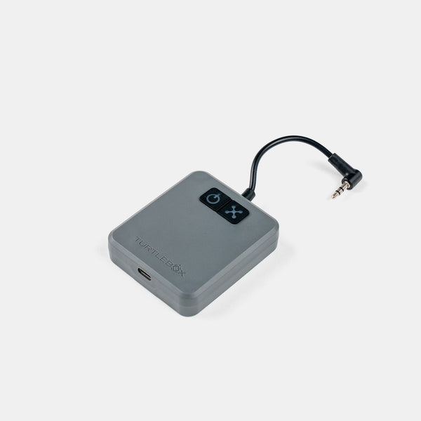 A gray rectangular electronic device with a black power button panel and a short black cable ending in a 3.5mm audio jack, shown on a light gray background.