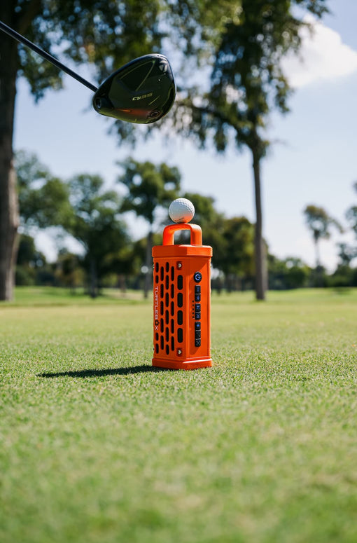 Golf club head with a golf ball on an orange Ranger Turtlebox speaker in a golf course setting
